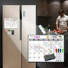 A refrigerator magnet calendar set shown attached to a stainless steel refrigerator, with a man preparing food in a kitchen in the background. The set includes a white monthly calendar, four markers in different colors, and a dark gray sponge.